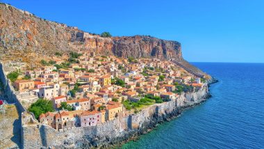 Spettacolare veduta aerea di Monemvasia, una città storica posizionata su una massiccia roccia nel Peloponneso. Il paesaggio mostra edifici in pietra tradizionali aggrappati al bordo della scogliera, testimoniando secoli di storia incastonata in questo luogo magnifico.