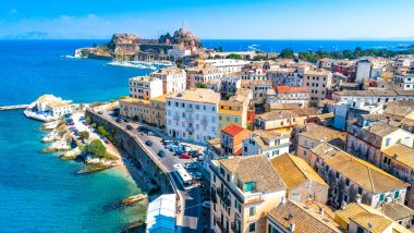 Panorama aereo della città storica di Corfù, mostrando l'antica architettura tra acque blu e l'antica fortezza su un promontorio.