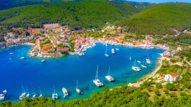 Vista aerea del porto di Fiscardo a Cefalonia, con yacht ormeggiati nell'acqua azzurra e case colorate che circondano la baia.