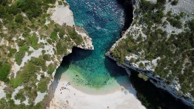 Isola di Vis Baia di Stiniva - Vista aerea della Baia di Stiniva, sull'isola di Vis, famosa per la sua stretta apertura tra alte scogliere che conduce a una spiaggia di ciottoli con acque turchesi e trasparenti, con alcune barche e visitatori che godono di questo angolo nascosto del paradiso.