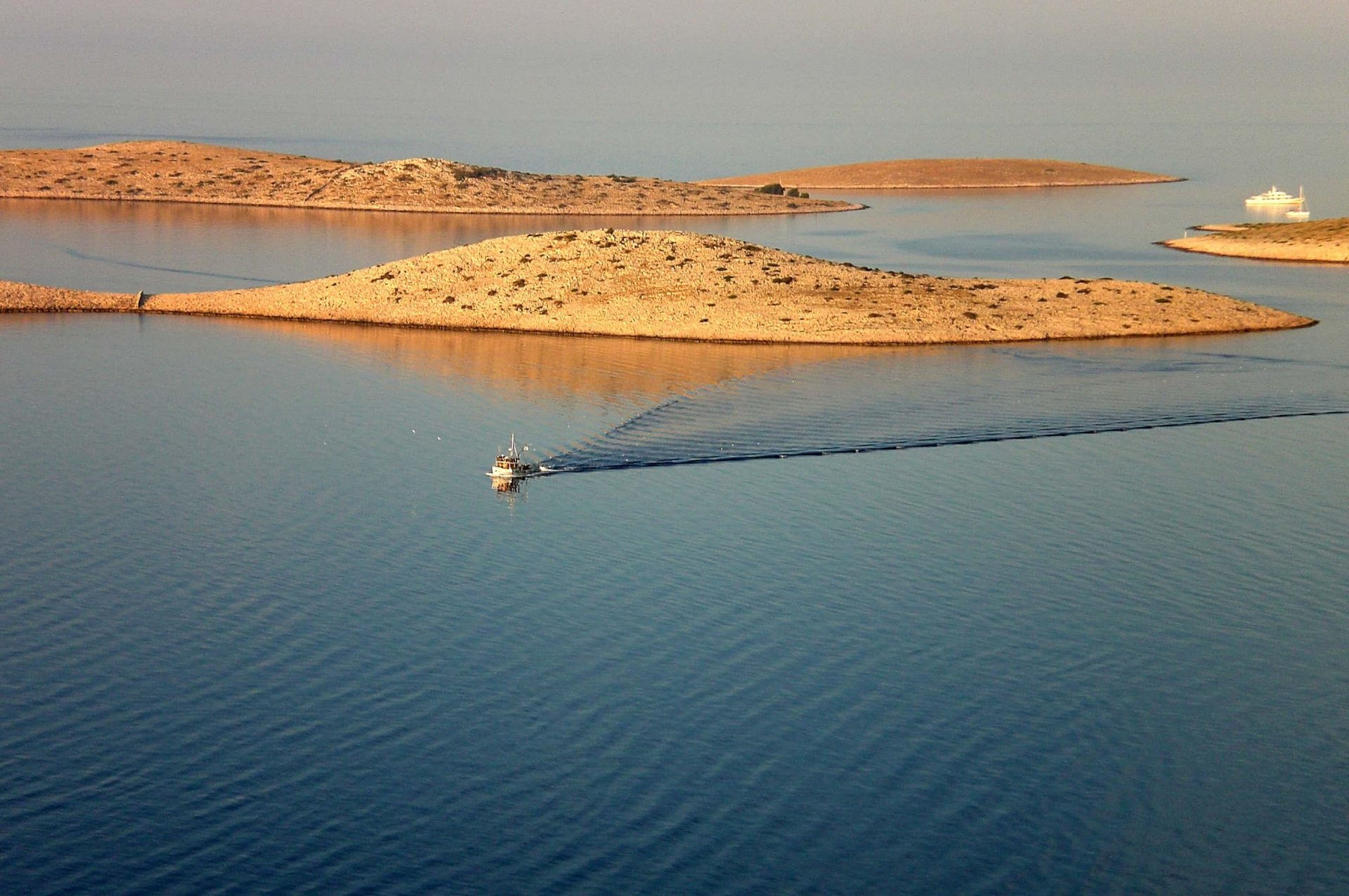 Le Isole Incoronate All'Alba, un peschereccio e sullo sfondo, tra le acque calme, una barca a vela.