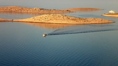 Le Isole Incoronate All'Alba, un peschereccio e sullo sfondo, tra le acque calme, una barca a vela.