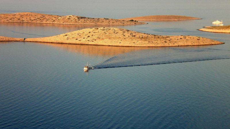 Le Isole Incoronate All'Alba, un peschereccio e sullo sfondo, tra le acque calme, una barca a vela.