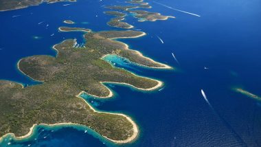 Vista aerea dell'arcipelago delle Isole Pakleni in Dalmazia, con sottili lingue di terra circondate da acque blu profondo, viste dall'alto, con barche a vela che tracciano bianche scie sull'acqua e sottolineano il contrasto con la rigogliosa vegetazione verde scuro.