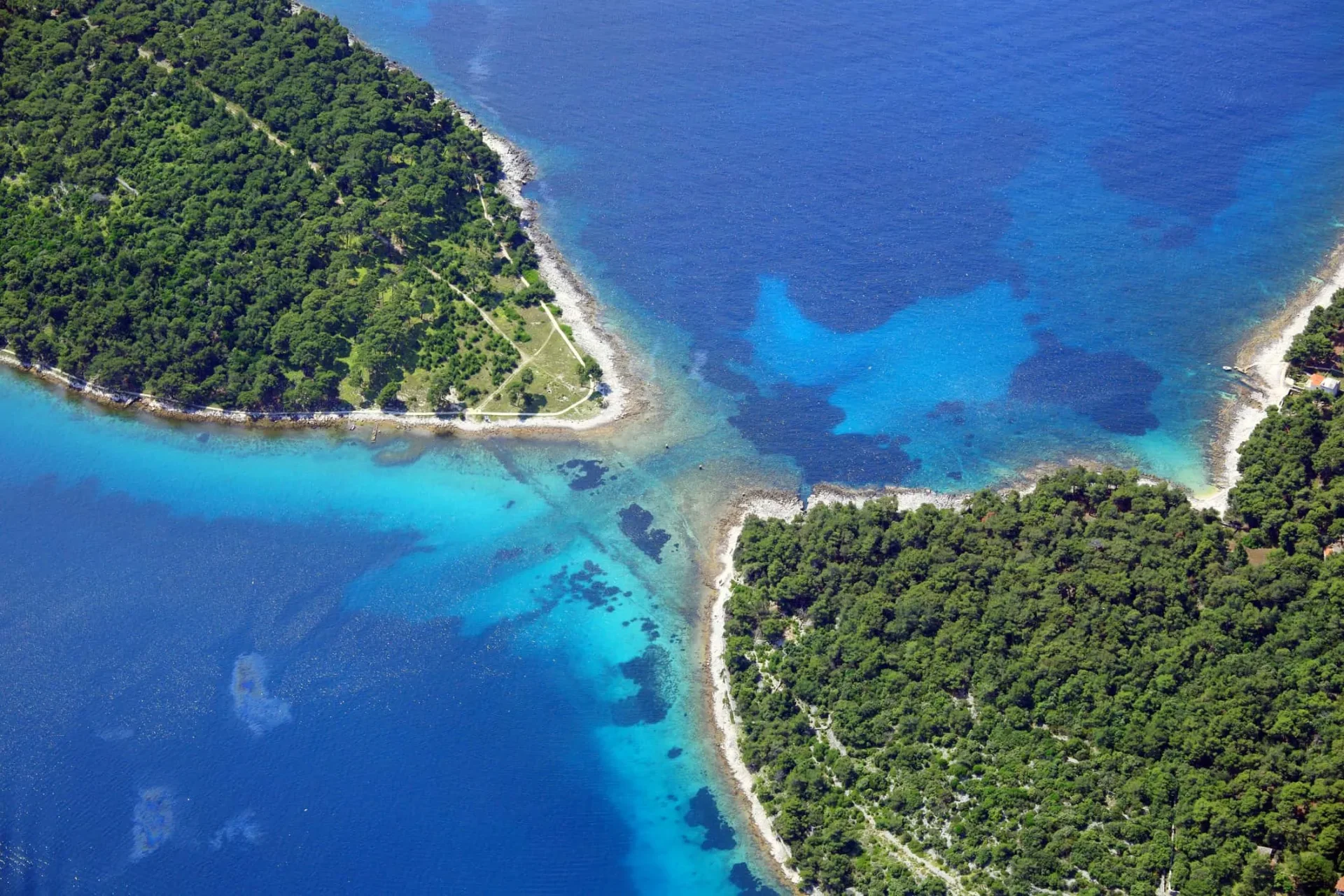 Istmo tra Lussino e Kludarac , vista aerea della penisola verde frangiata da acque cristalline e spiagge appartate nell'arcipelago istriano.