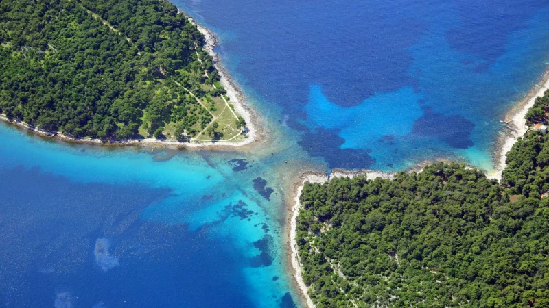 Istmo tra Lussino e Kludarac , vista aerea della penisola verde frangiata da acque cristalline e spiagge appartate nell'arcipelago istriano.